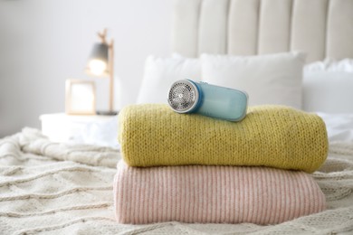 Photo of Modern fabric shaver and woolen sweaters on bed indoors