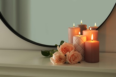 Burning candles and roses on white console table near mirror, space for text