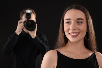 Photo of Professional photographer taking picture of beautiful young woman on black background, selective focus