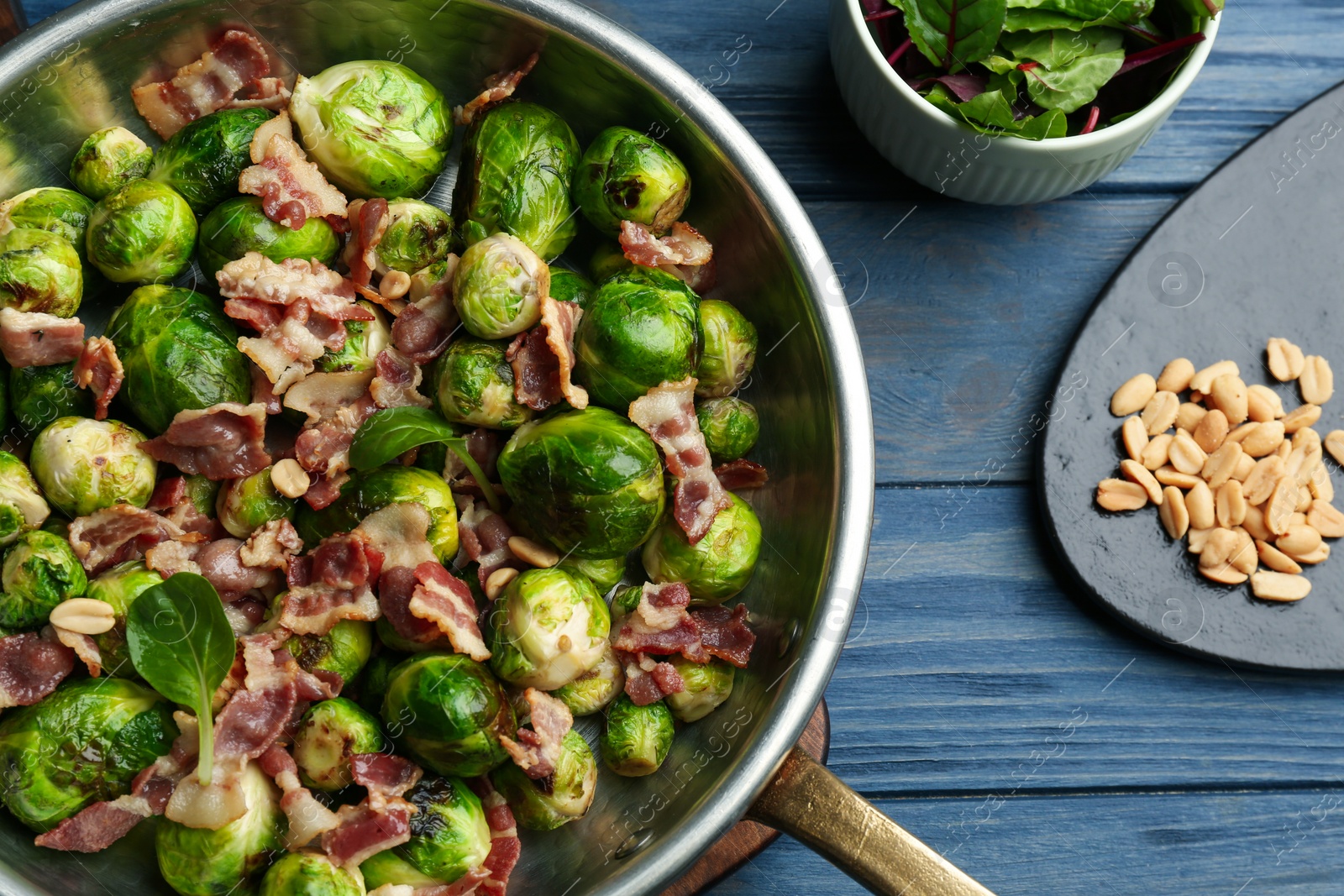 Photo of Delicious Brussels sprouts with bacon on blue wooden table, flat lay