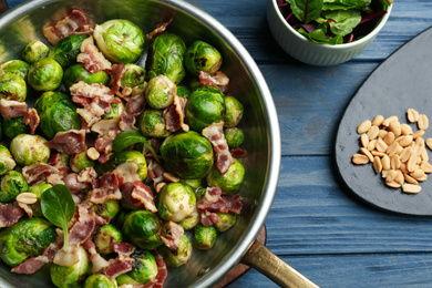 Delicious Brussels sprouts with bacon on blue wooden table, flat lay