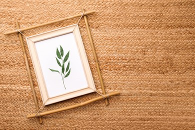 Photo of Bamboo frame with green twig on wicker straw background, top view. Space for text