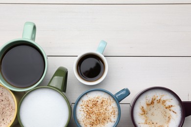 Photo of Many different cups with aromatic hot coffee on white wooden table, flat lay. Space for text