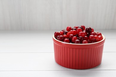 Photo of Fresh ripe cranberries in bowl on white wooden table, closeup. Space for text