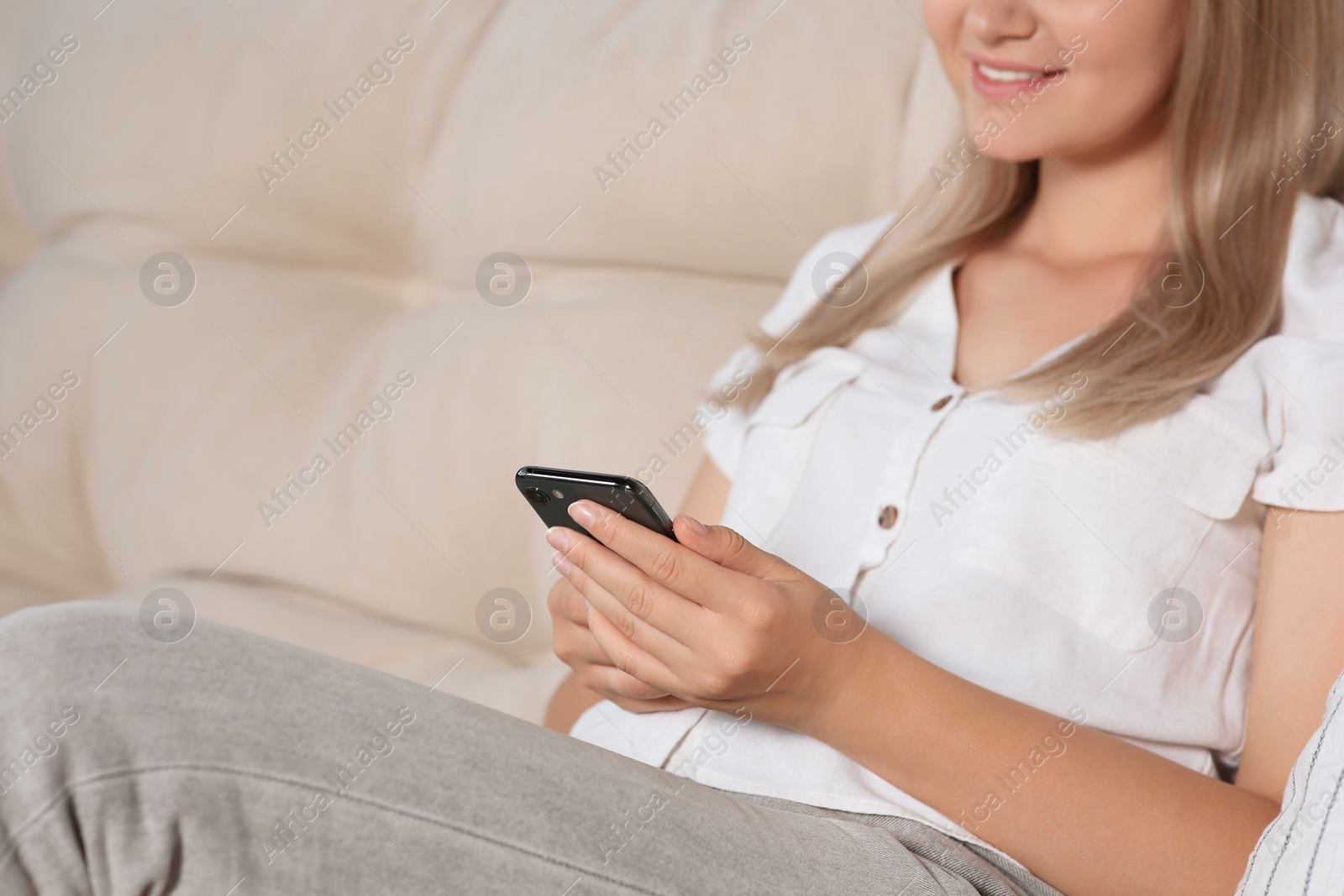 Photo of Woman using smartphone on sofa at home, closeup