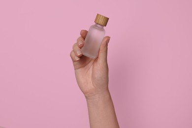 Photo of Woman holding bottle of cosmetic product on pink background, closeup