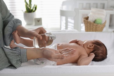 Photo of Mother with bottle of massage oil near baby on changing table at home, closeup