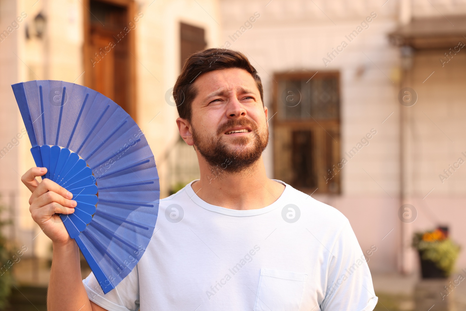 Photo of Man with hand fan suffering from heat outdoors