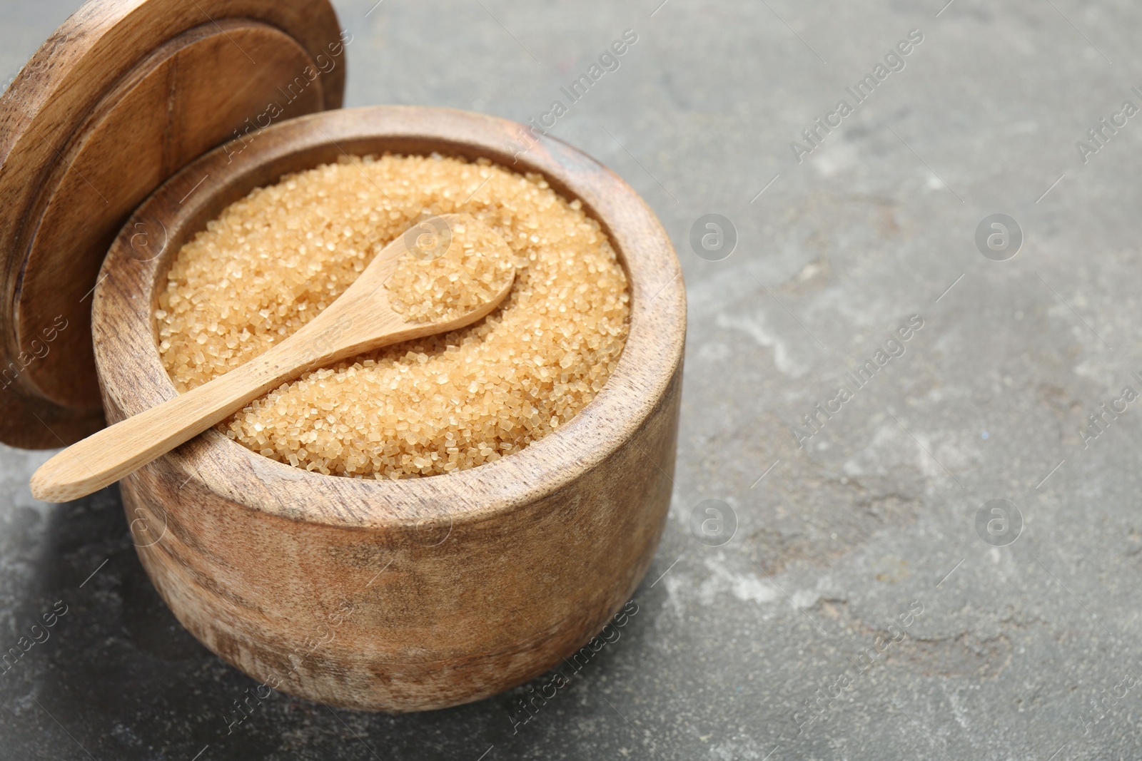 Photo of Brown sugar in bowl and spoon on grey textured table, closeup. Space for text