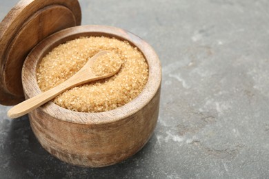 Brown sugar in bowl and spoon on grey textured table, closeup. Space for text