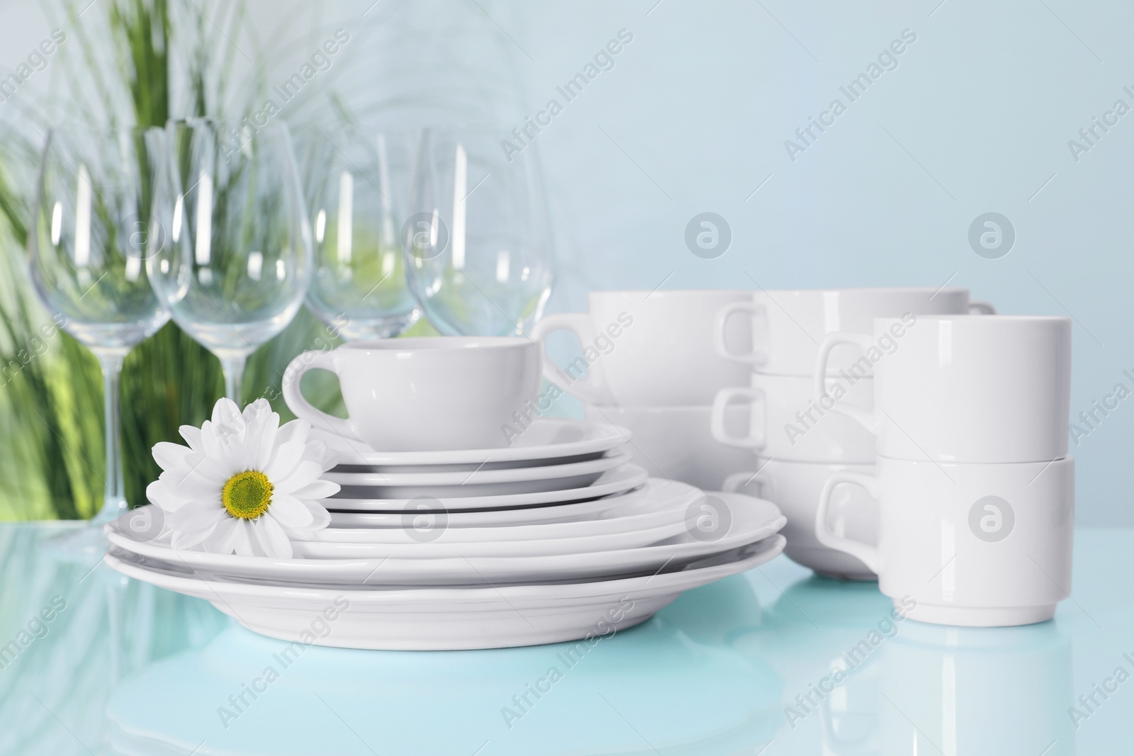 Photo of Set of clean dishware and flower on light blue table, closeup