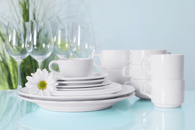 Set of clean dishware and flower on light blue table, closeup