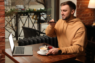 Male blogger taking photo of dessert and coffee at table in cafe