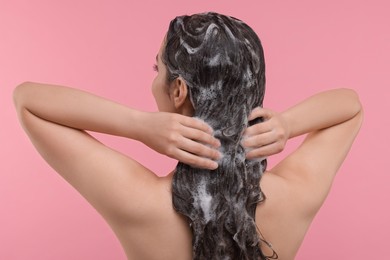 Woman washing hair on pink background, back view