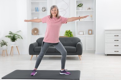 Photo of Senior woman in sportswear doing exercises on mat at home
