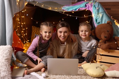 Mother and her children with laptop in play tent at home