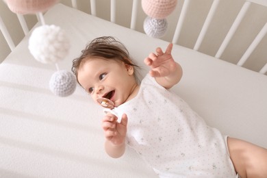 Cute little baby lying in crib with hanging mobile