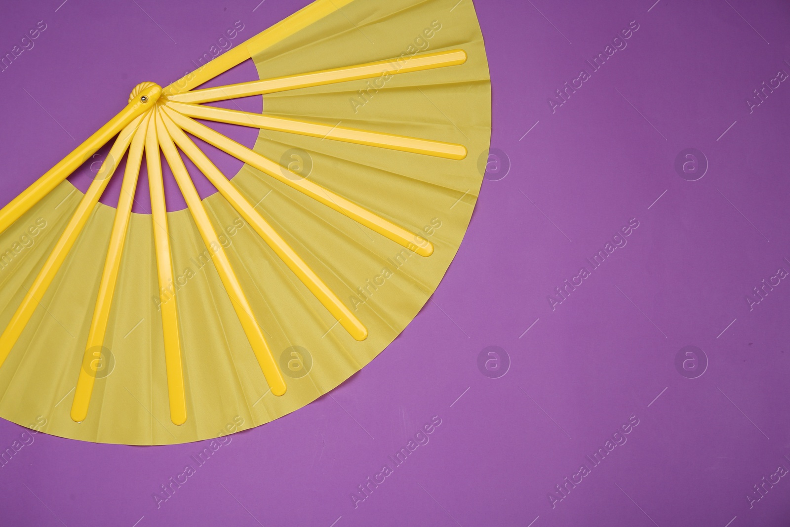 Photo of Bright yellow hand fan on purple background, top view. Space for text