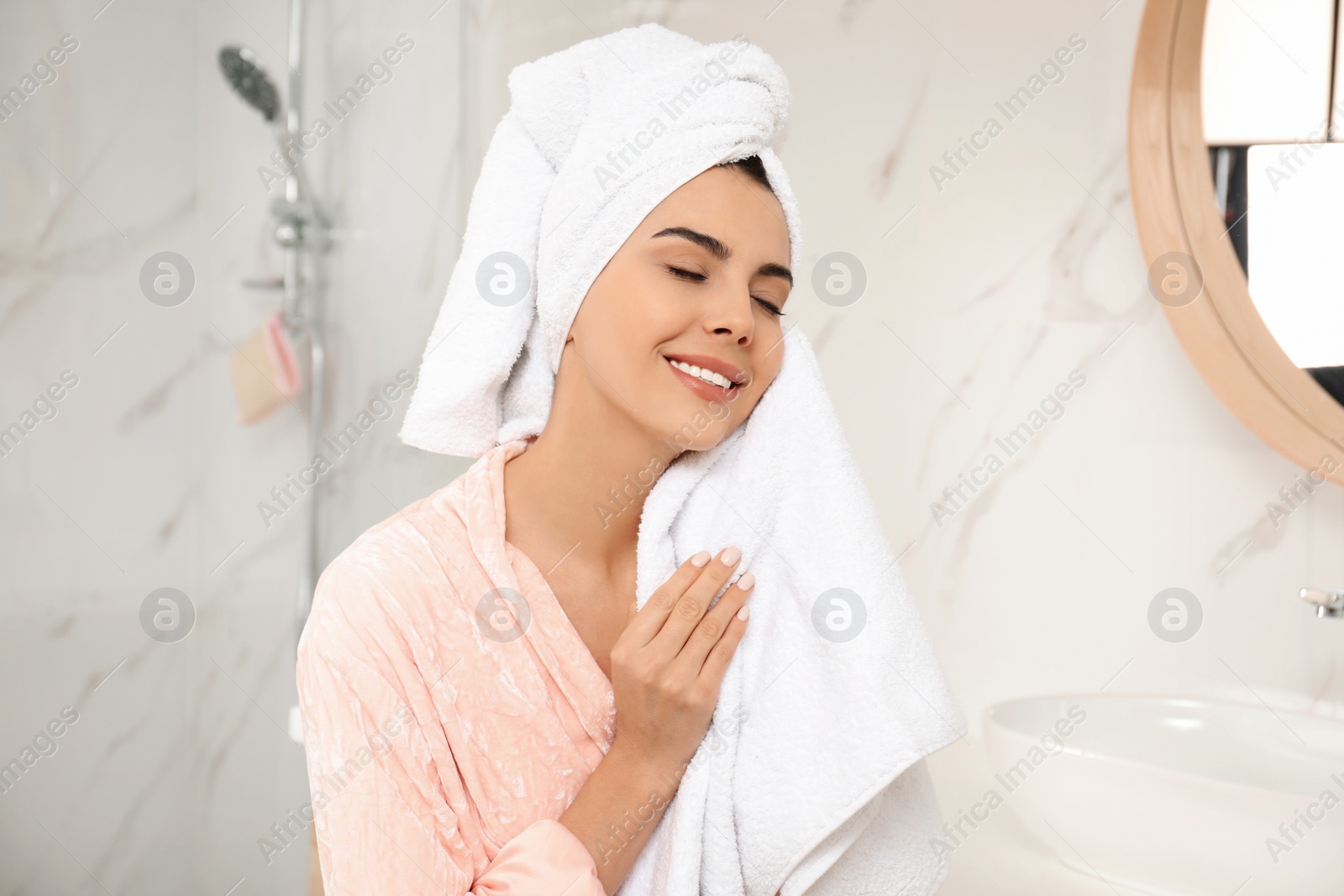 Photo of Young woman wiping face with towel in bathroom