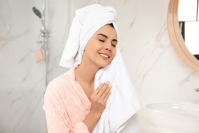 Photo of Young woman wiping face with towel in bathroom