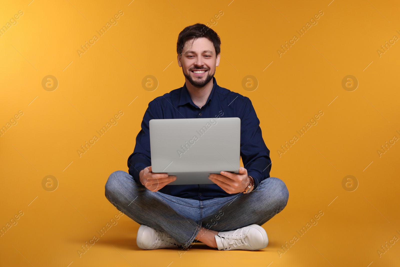Photo of Happy man with laptop sitting on yellow background