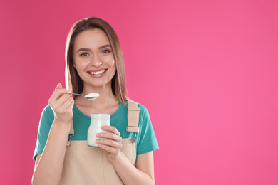 Young attractive woman with tasty yogurt on pink background. Space for text