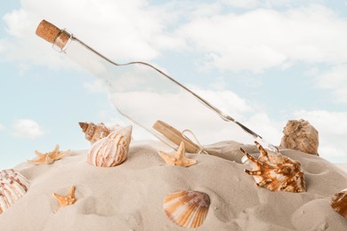 Photo of Corked glass bottle with rolled paper note and seashells on sand against sky