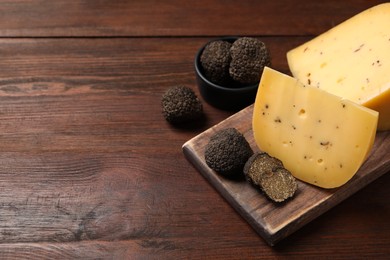 Photo of Delicious cheese and fresh black truffles on wooden table. Space for text