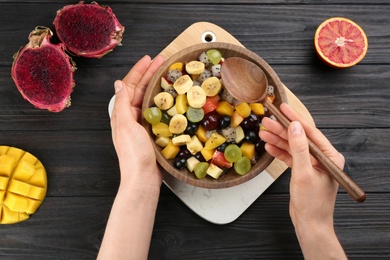Photo of Woman with delicious exotic fruit salad at black wooden table, top view