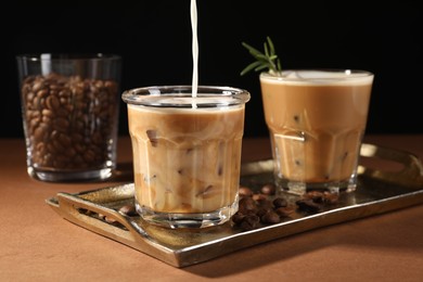 Photo of Pouring milk into glass with refreshing iced coffee at brown table