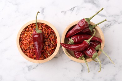 Photo of Chili pepper flakes and pods on white marble table, top view