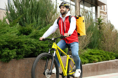 Courier with thermo bag riding bicycle outdoors. Food delivery service