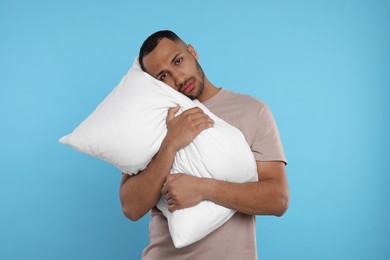 Tired man with pillow on light blue background. Insomnia problem