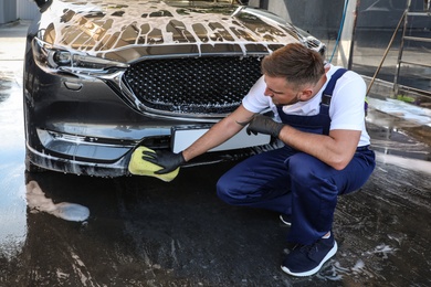Photo of Young worker cleaning automobile with sponge at car wash