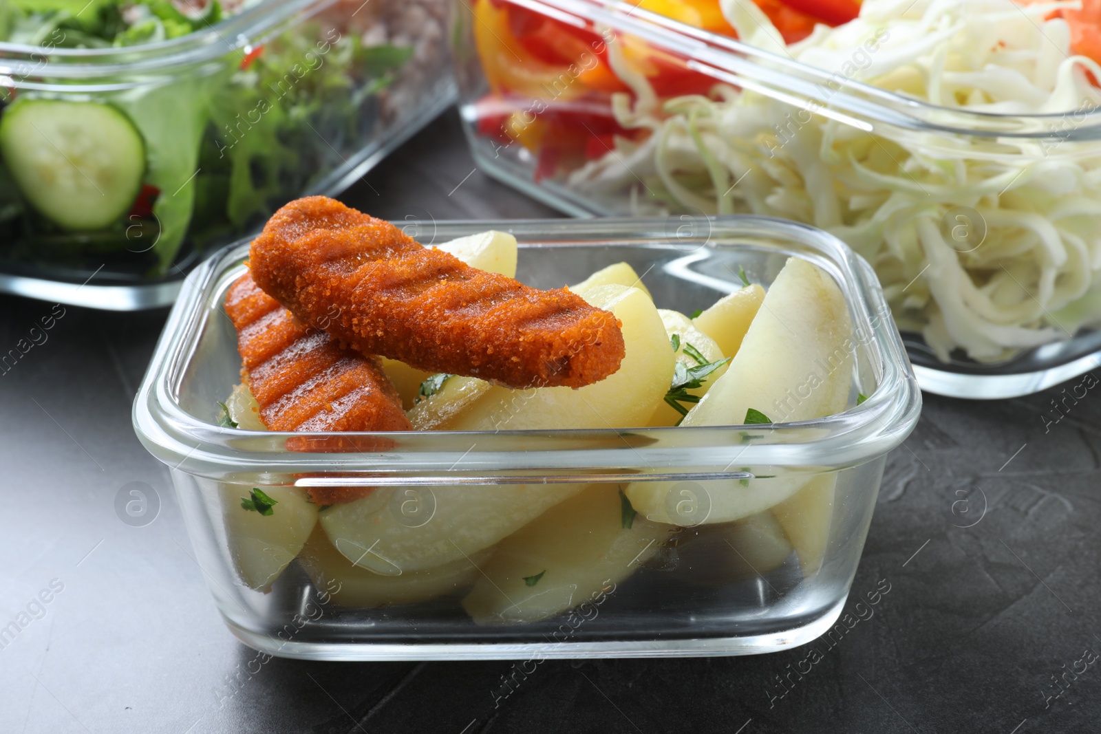 Photo of Tasty potatoes with cutlets in glass container on grey table