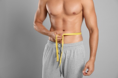 Photo of Young man with slim body using measuring tape on grey background, closeup view