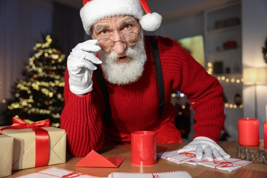 Photo of Santa Claus looking into camera at his workplace in room decorated for Christmas