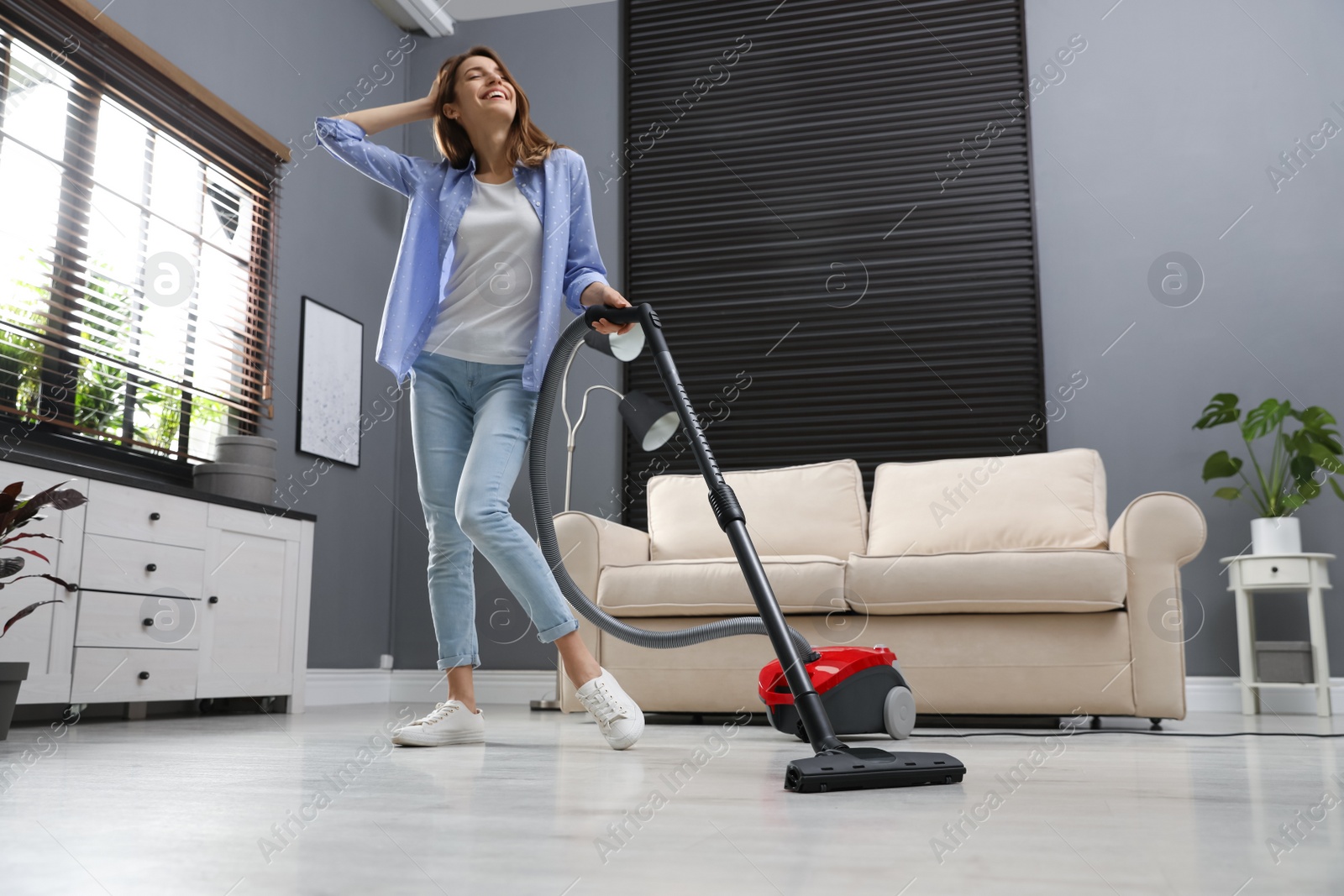 Photo of Young woman having fun while vacuuming at home