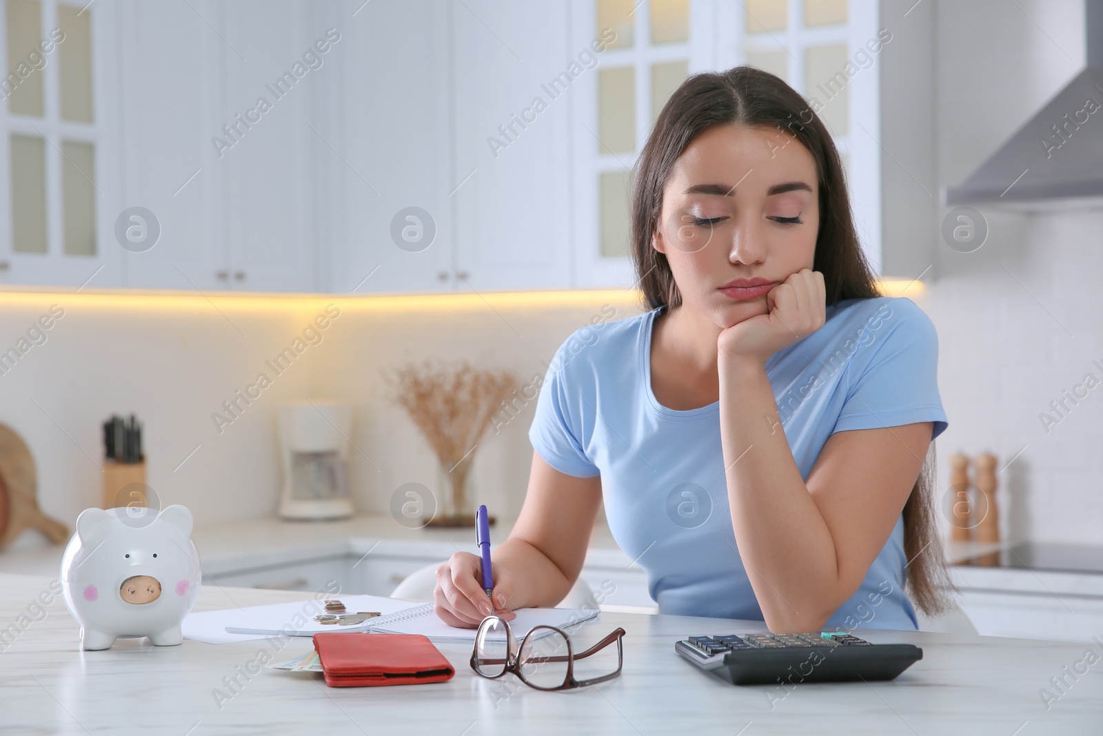 Photo of Sad young woman counting money with calculator at table in kitchen, space for text