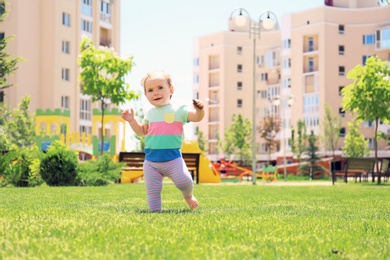 Cute baby girl learning to walk outdoors on sunny day