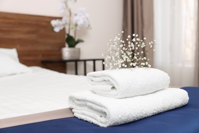 Stack of clean towels with flowers on bed in hotel room