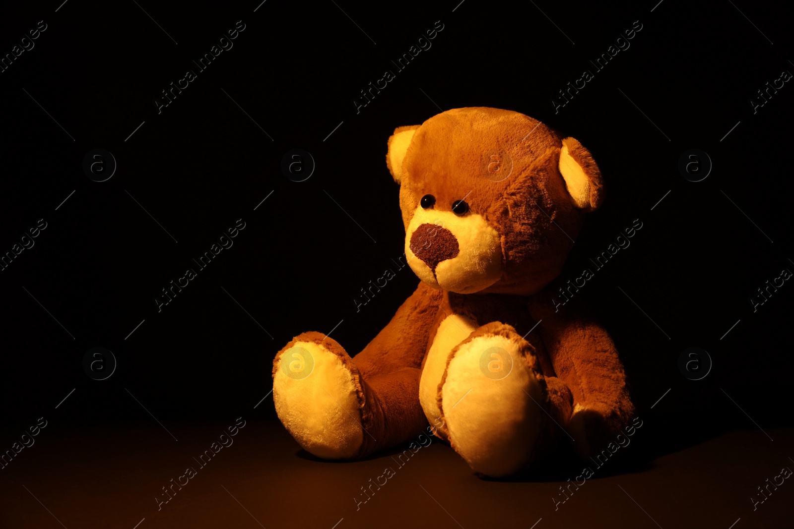 Photo of Cute lonely teddy bear on dark background. Space for text