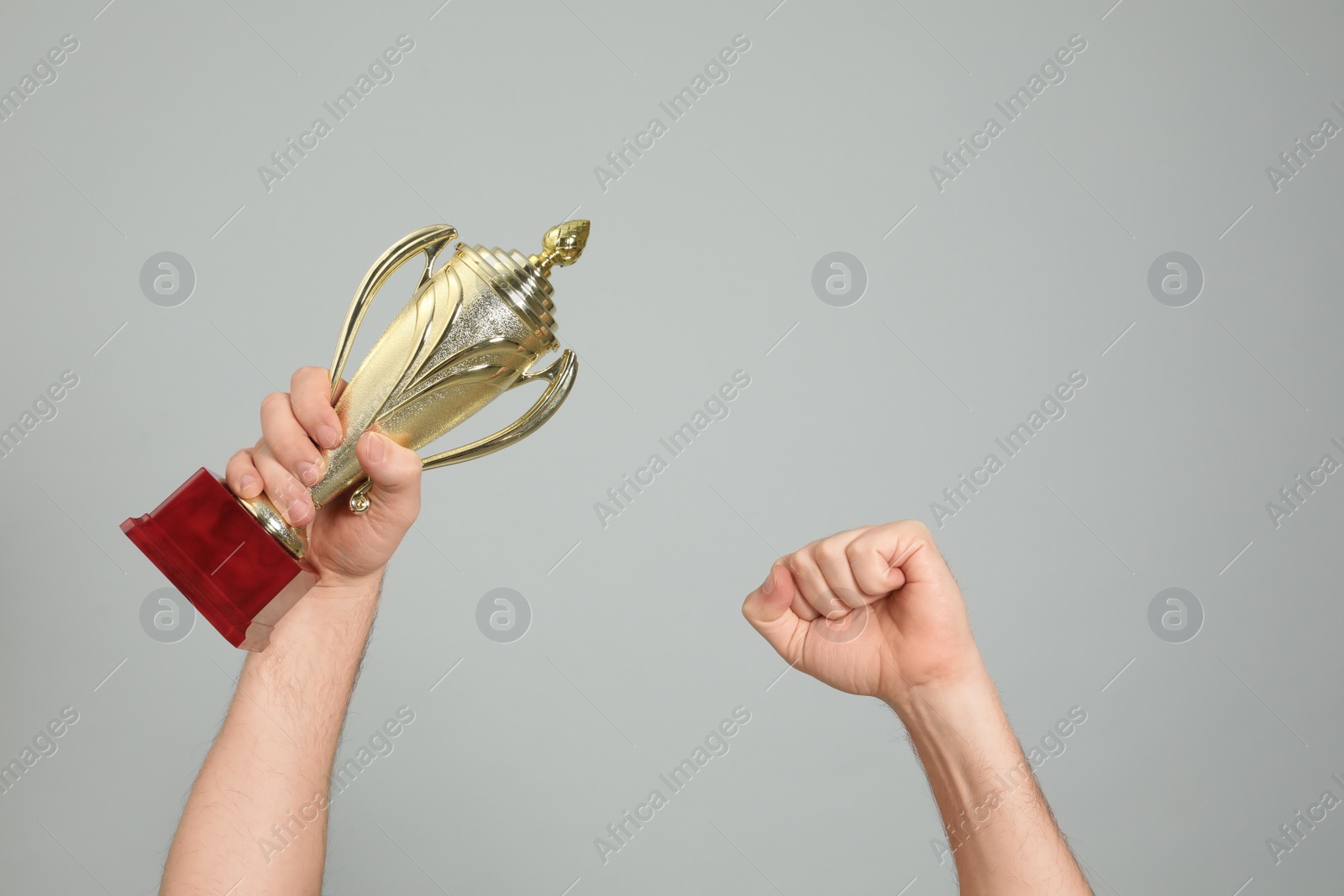 Photo of Man holding gold trophy cup on light grey background, closeup