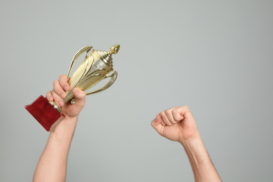 Man holding gold trophy cup on light grey background, closeup