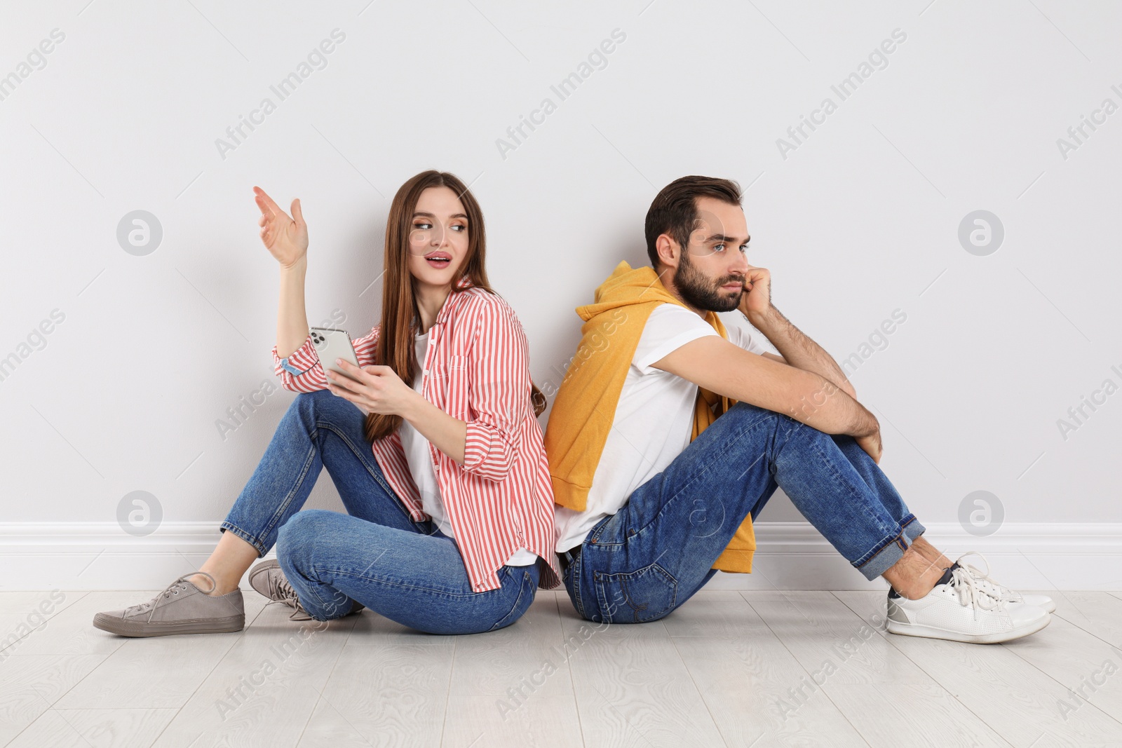 Photo of Woman with smartphone mocking her boyfriend indoors. Relationship problems