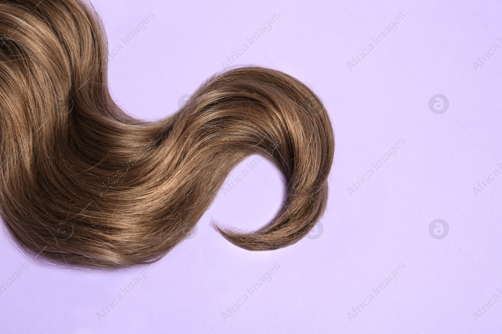 Photo of Lock of brown wavy hair on color background, top view. Space for text