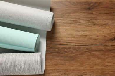 Photo of Different wallpaper rolls on wooden table, flat lay. Space for text