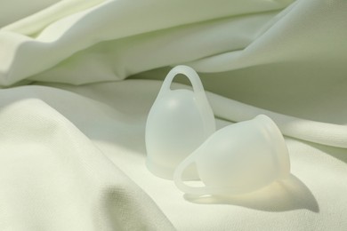 Photo of Menstrual cups on light fabric. Space for text