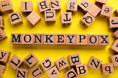 Photo of Word Monkeypox and many wooden cubes on yellow background, flat lay