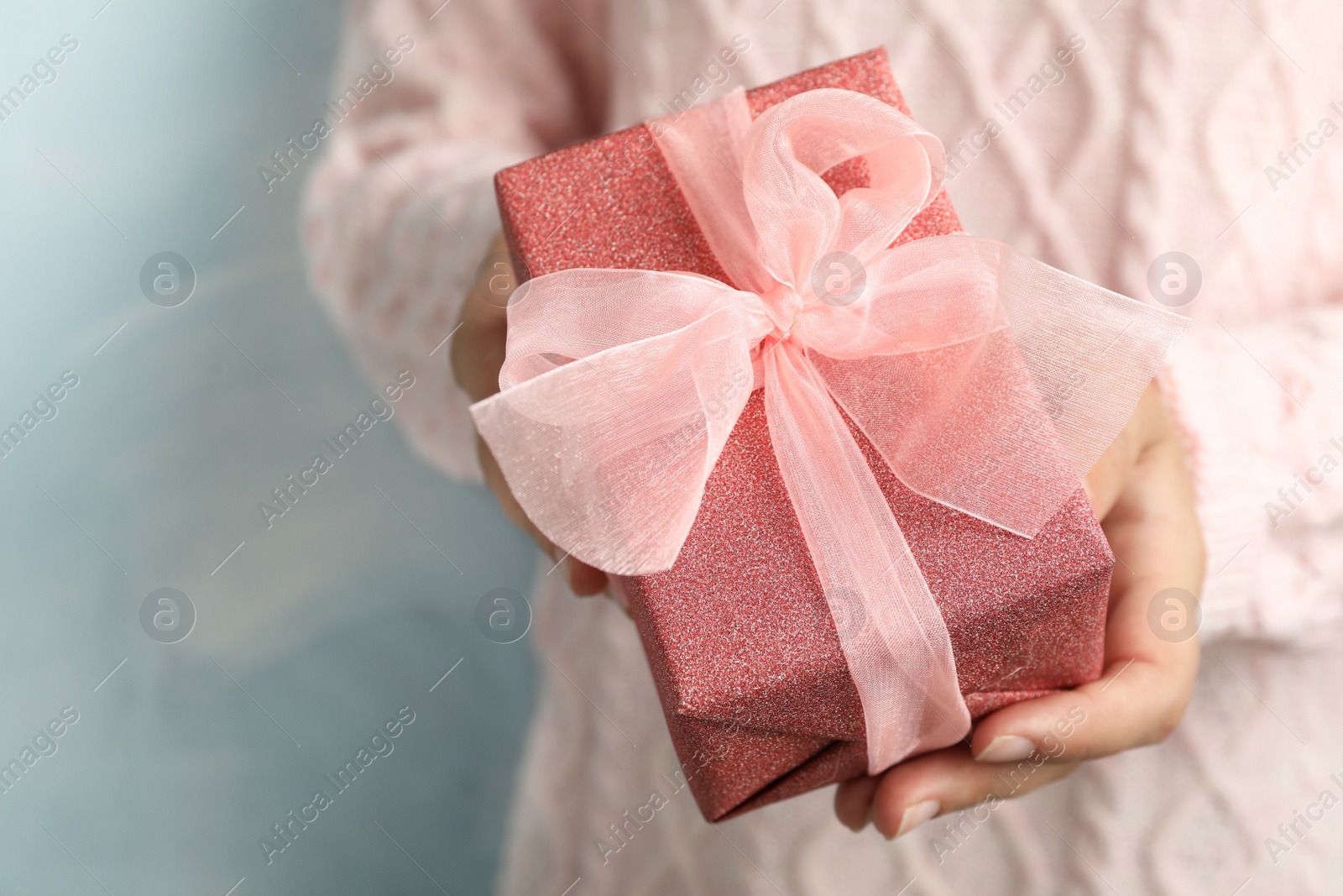 Photo of Woman holding beautiful Christmas gift on light blue background, closeup